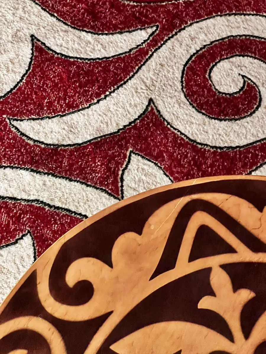 Close-up of red and white Kazakh ornamental carpet pattern beside a carved wooden table edge